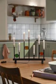 Candelabra 7 Lights Zwart Van Konstsmide - De zeven kaarsen zijn omlijst met decoratieve gekleurde glazen details in groen, rood en amber, waardoor een elegante en feestelijke sfeer ontstaat.