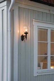 Orion Zwart buitenlamp Van Konstsmide - Met zijn decoratieve details en tijdloze stijl wordt deze wandlamp een elegant detail dat uw gevel verfraait en een uitnodigende sfeer creëert.