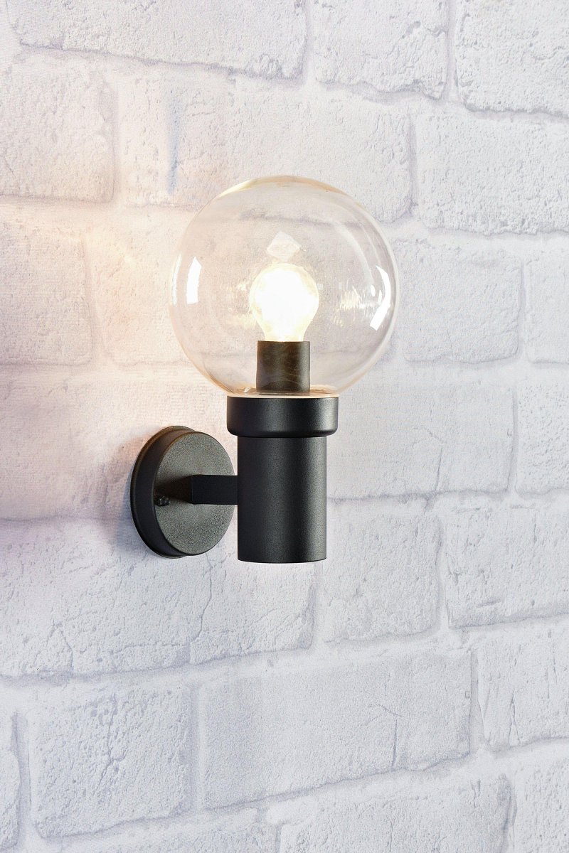Caris Zwart buitenlamp Van Markslöjd - Met een robuuste, zwarte metalen voet en een grote, heldere glazen kap verspreidt de lamp een helder en aangenaam licht dat een uitnodigende sfeer cre&euml;ert.