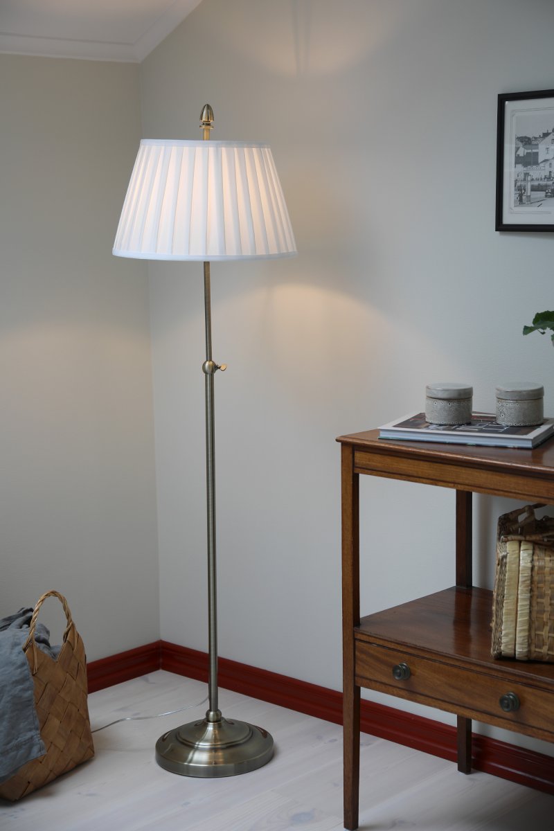 Oxford Antiek messing vloerlamp Van Markslöjd - Staande lamp in klassieke stijl van rond de eeuwwisseling met een gebroken witte stoffen kap en een voet met een antiek messing afwerking.