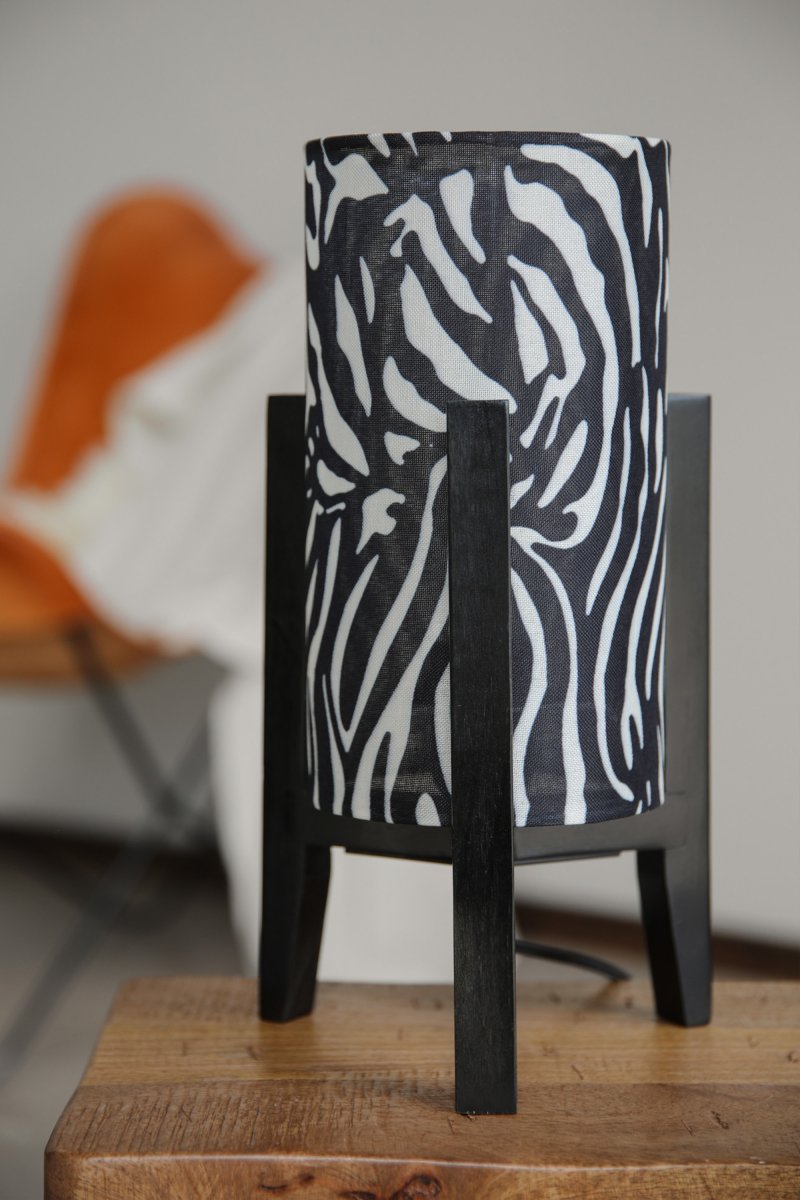 Eruca 34cm Zebra tafellamp Van Markslöjd - De zwarte houten lampvoet is gecombineerd met een cilindrische textielen kap in een zwart-wit zebraprint, wat de lamp een grafisch en expressief karakter geeft.
