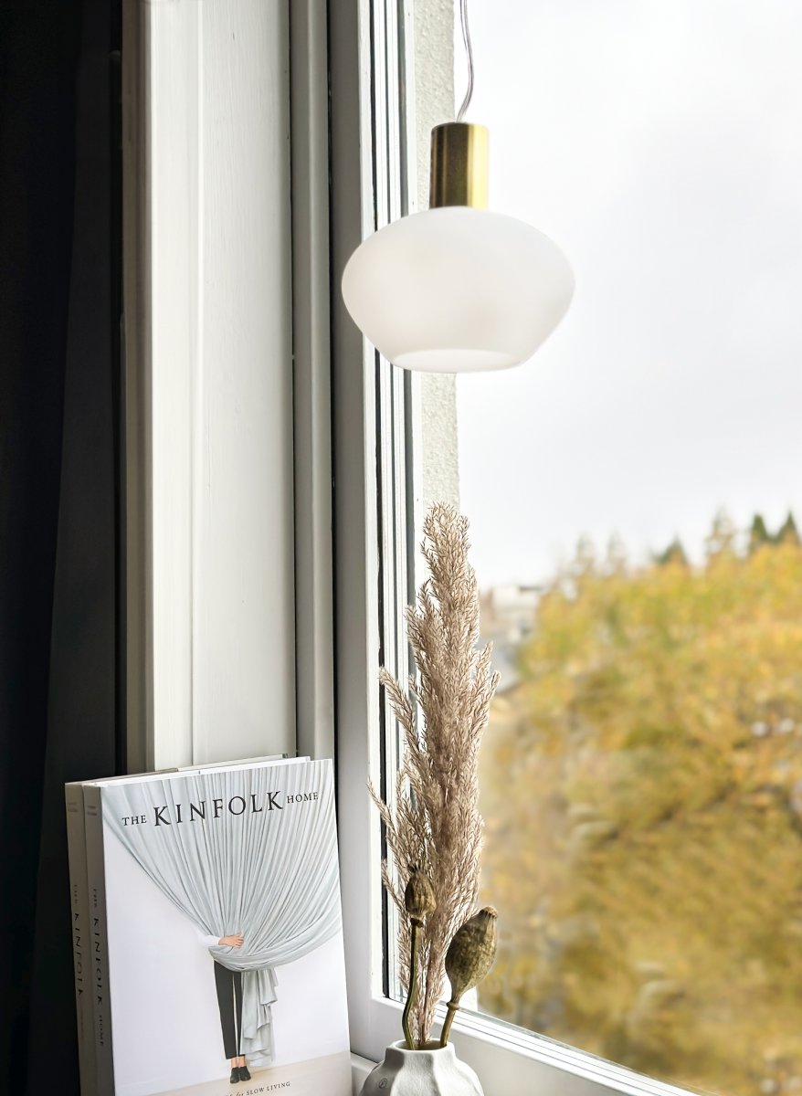 Bell Ø15 Wit raamlamp Van Aneta Lighting - Gemaakt van metaal met een matte messing afwerking en een ronde kap van opaalglas die een zachte en aangename gloed verspreidt.