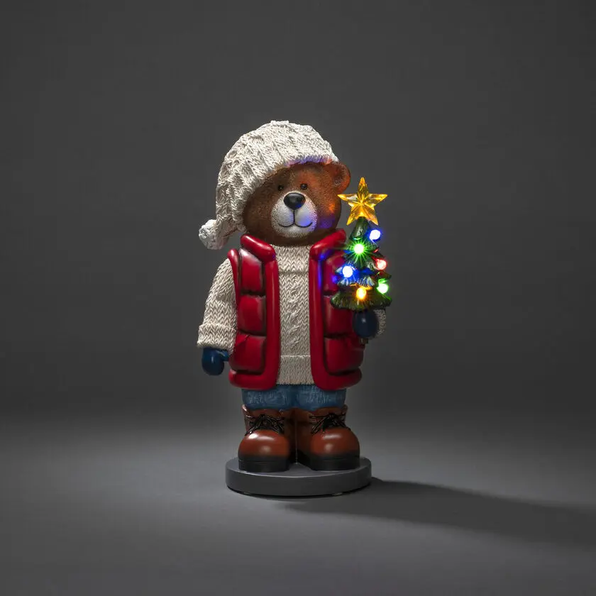 Kleine Teddybeer 38cm Veelkleurig Van Konstsmide - Er staat een felverlichte kerstboom en een lantaarn in, wat voor een gezellige sfeer zorgt.