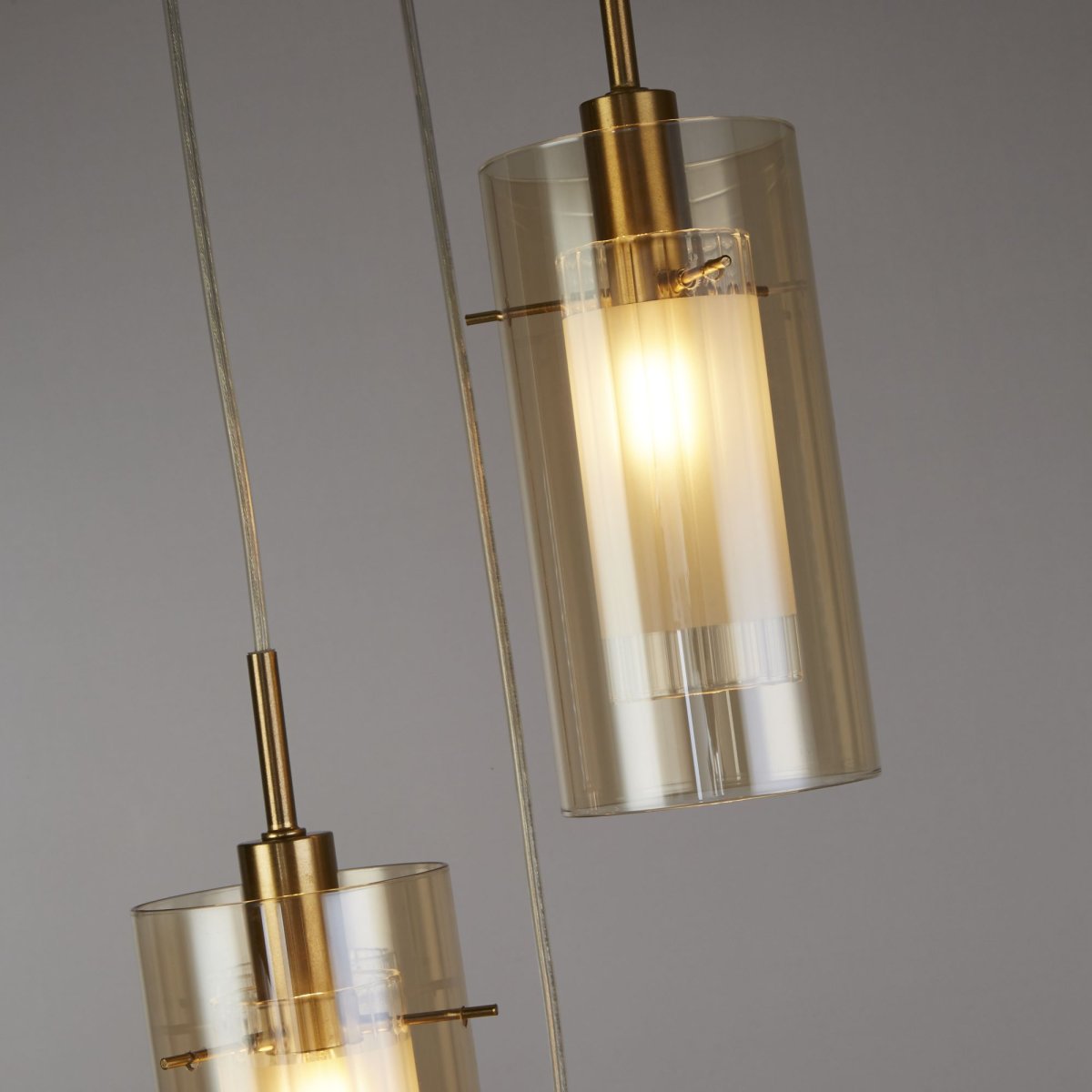 Duo Ø26 Bronzen hanglamp Van Searchlight - De lamp is gemaakt van metaal met een stijlvolle bronzen afwerking en heeft drie cilindrische glazen kappen van amberkleurig glas.