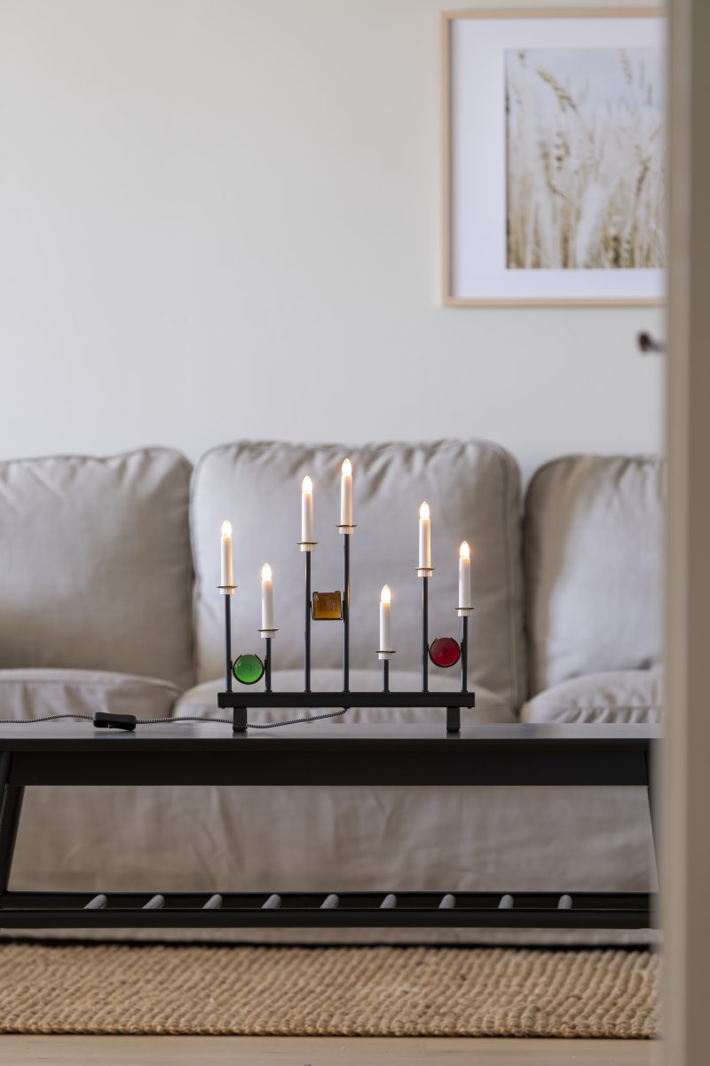 Candelabra 7 Lights Zwart Van Konstsmide - De zeven kaarsen zijn omlijst met decoratieve gekleurde glazen details in groen, rood en amber, waardoor een elegante en feestelijke sfeer ontstaat.