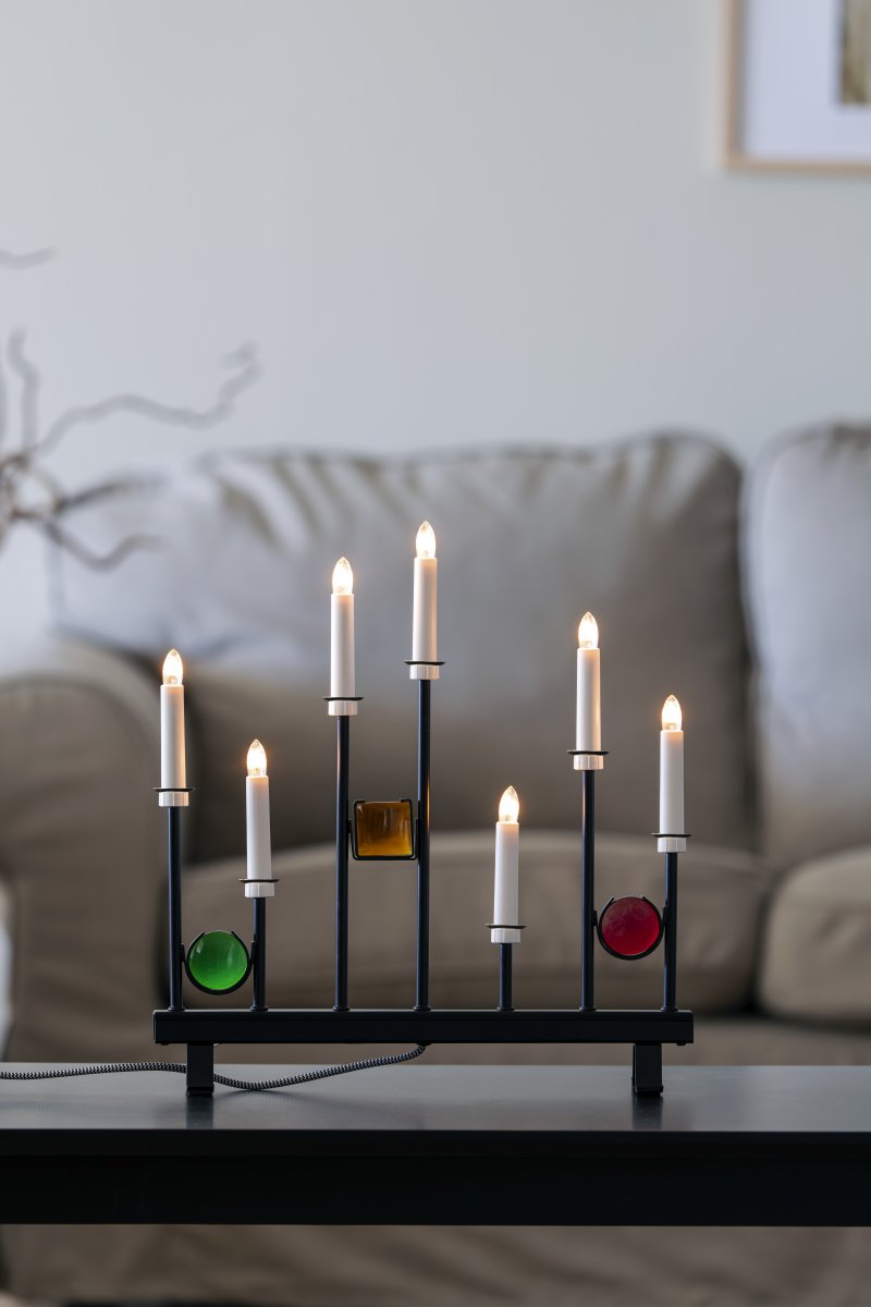 Candelabra 7 Lights Zwart Van Konstsmide - De zeven kaarsen zijn omlijst met decoratieve gekleurde glazen details in groen, rood en amber, waardoor een elegante en feestelijke sfeer ontstaat.