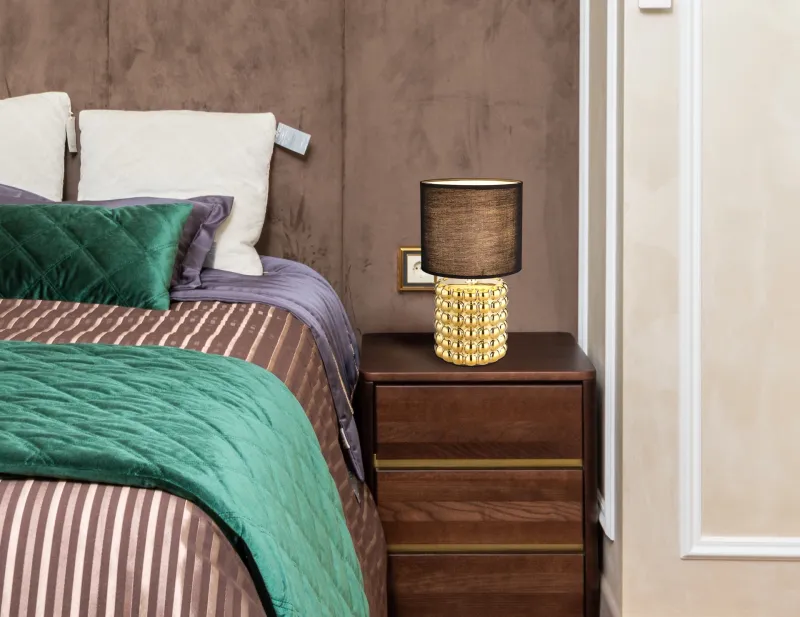 Valentino 33cm Goud tafellamp Van Globo Lighting - P&aring; en cylinderformad fot i guldf&auml;rgad keramik vilar en stilren, svart textilsk&auml;rm.