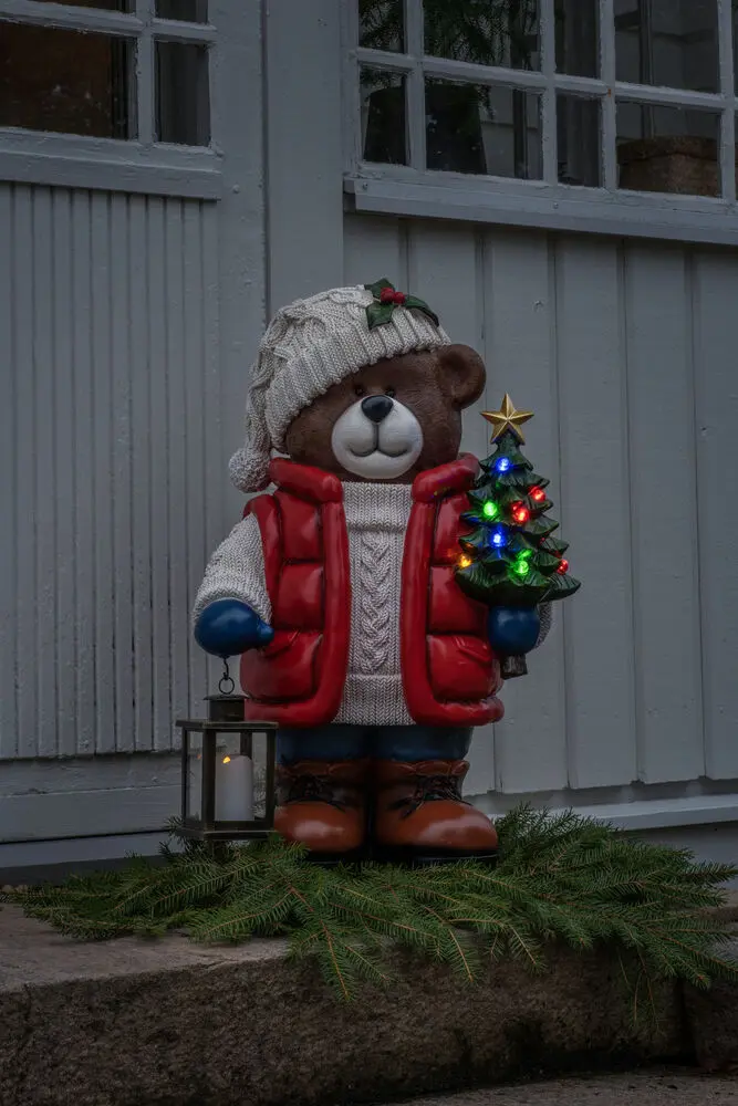Grote Teddybeer 66cm Veelkleurig Van Konstsmide - Er staat een felverlichte kerstboom en een lantaarn in, wat voor een gezellige sfeer zorgt.