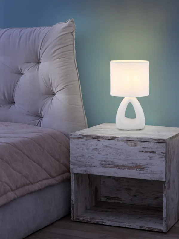 Triangle 30cm Wit tafellamp Van Globo Lighting - Den triangelformade basen med ett stilrent utskuret h&aring;l ger ett modernt intryck, medan den ovala textilsk&auml;rmen i vit f&auml;rg sprider ett behagligt och j&auml;mnt ljus.