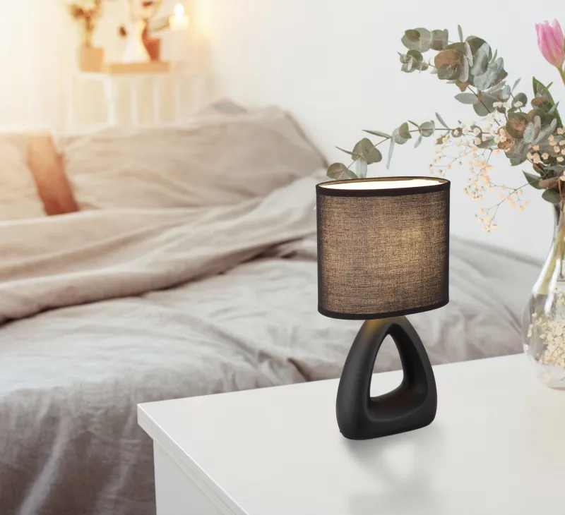 Triangle 30cm Zwart tafellamp Van Globo Lighting - Den triangelformade basen med ett stilrent utskuret h&aring;l ger ett modernt intryck, medan den ovala textilsk&auml;rmen i svart f&auml;rg sprider ett behagligt och j&auml;mnt ljus.