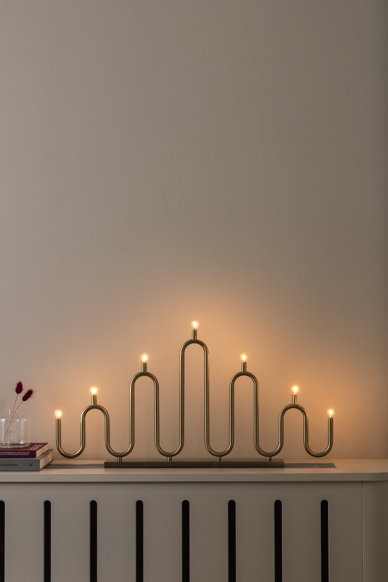 Noel 7 Messing Van Globen Lighting - Het zachte, golvende ontwerp is gemaakt van metalen buizen die met de hand op verschillende niveaus zijn gebogen en biedt een moderne interpretatie van de klassieke adventskaarsenhouder.