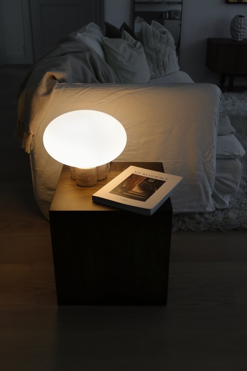 Mammut 25cm Travertijn tafellamp Van Globen Lighting - De lampenvoet is gecombineerd met een ronde, matwitte en afgeplatte glazen kap in een iets groter formaat, wat een speelse uitstraling creëert.