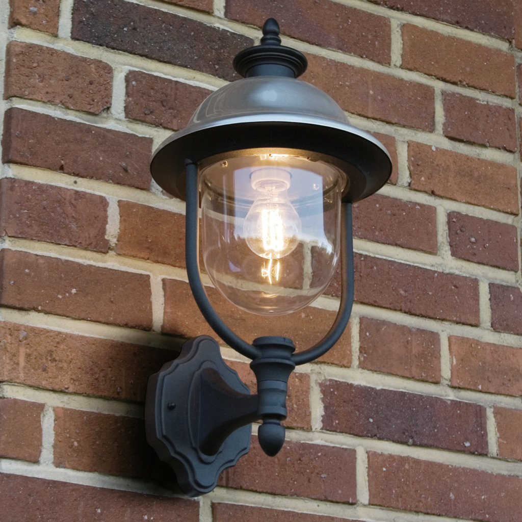 Parma Zwart buitenlamp Van Konstsmide - Dankzij de robuuste zwarte afwerking en de kap van helder glas verspreidt het een warm en uitnodigend licht, wat een uitnodigende sfeer creëert bij de entree of op het terras.