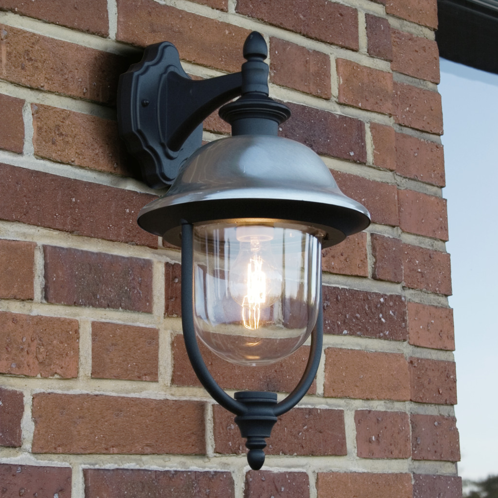 Parma Zwart buitenlamp Van Konstsmide - Dankzij de robuuste zwarte afwerking en de kap van helder glas verspreidt het een warm en uitnodigend licht, wat een uitnodigende sfeer creëert bij de entree of op het terras.