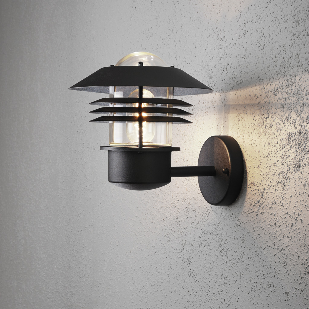 Modena Zwart buitenlamp Van Konstsmide - Dankzij het beschermende dak en het stijlvolle design zorgt het voor een aangenaam en gericht licht, ideaal voor het creëren van een veilige en uitnodigende sfeer buitenshuis.
