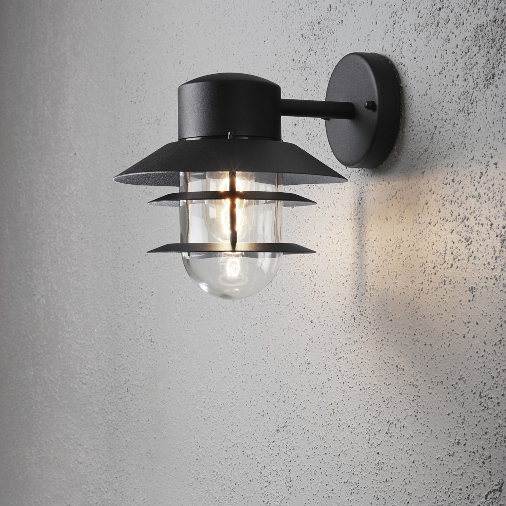 Modena Zwart buitenlamp Van Konstsmide - Dankzij het beschermende dak en het stijlvolle design zorgt het voor een aangenaam en gericht licht, ideaal voor het creëren van een veilige en uitnodigende sfeer buitenshuis.