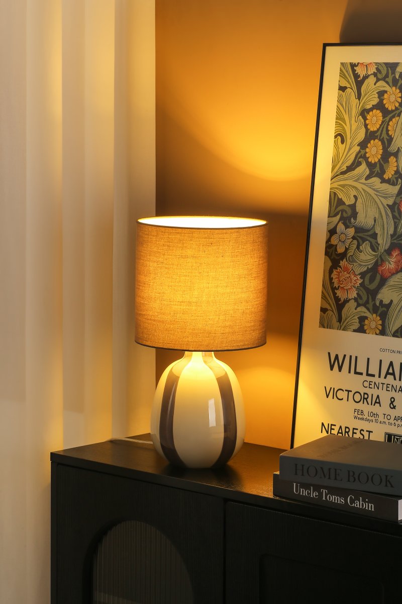 Rippel 40cm Grijs tafellamp Van Nordic Lighting - De lampvoet is gemaakt van keramiek met een cr&egrave;mekleurige basis en grijze strepen die een levendige maar zachte uitstraling geven.