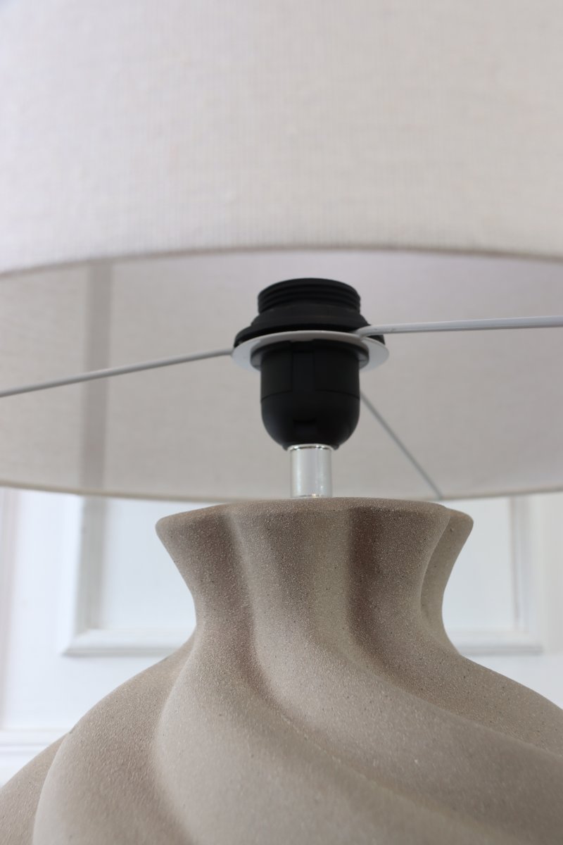 Vindel 52cm Zand tafellamp Van Lampan - De keramische lampvoet heeft een zandkleurig, gestructureerd oppervlak en een zacht, wervelend ontwerp dat een levendige en sculpturale uitstraling geeft.